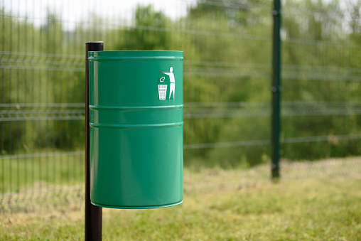 A green metal trash bin in the park or outside of a public utility building