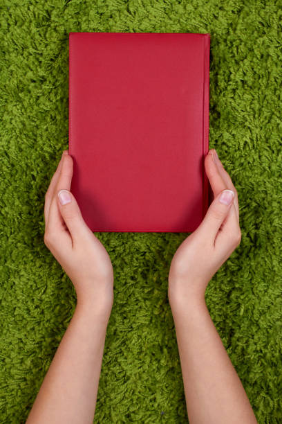 istock Woman's hands holding a red  book isolated on green background. 688144054