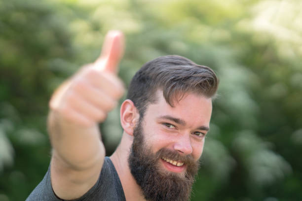 istock Handsome smiling guy with beard man doing thumbs up gesture. Selective focus on his face on background 688160200