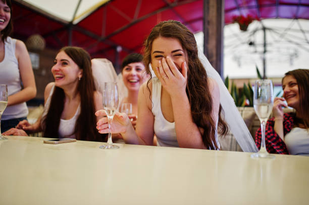 gruppe von fröhlichen mädchen in weißen hemden sitzen am tisch und trinken champagner am junggesellinnenabschied. - bachelorette party stock-fotos und bilder