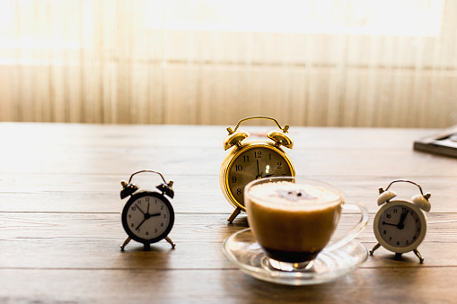 Vintage alarm clock with cup of coffee on wooden background