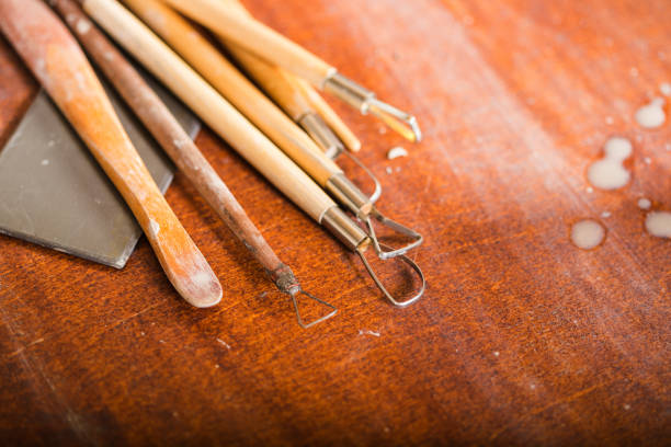 pottery, workshop, ceramics art concept - closeup on sculpting tools set on wooden table, clay stacks, different profiles, cutters for carving shapes