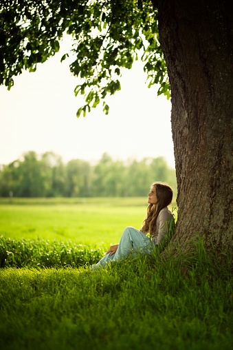 Beautiful caucasian women with long brown hair sit and relax under a chestnut-tree. Vibrant colors - evening sun.