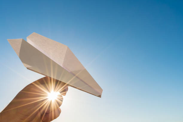 istock Hand holds white paper plane on blue sky and sun 688236858