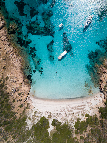 Aerial view of a boat in front of the Mortorio island in Sardinia. Amazing beach with a turquoise and transparent sea. Emerald Coast, Sardinia, Italy.