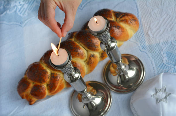 Shabbat eve Shabbat eve table.Woman hand lit Shabbath candles with uncovered challah bread and kippah. religious service photos stock pictures, royalty-free photos & images