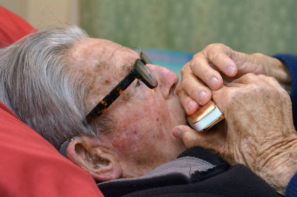 Old man plays a harmonica Old man plays a harmonica in bed. Concept photo of old age, lonely, alone, retirement, music, sad. harmonica stock pictures, royalty-free photos & images