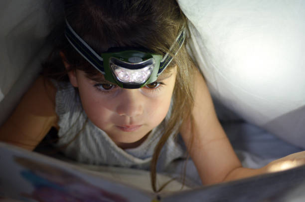 istock Little child reads book in bed under the covers at night 688300866