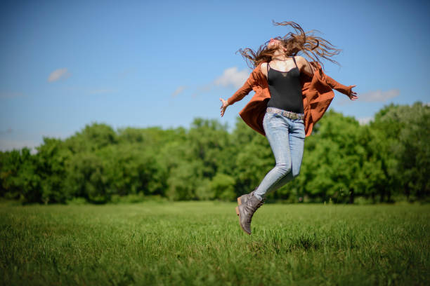 Young woman jumping from joy in the green park on a bright, sunny, summer day, enjoying life and youth