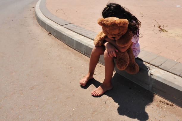 A young girl who is a victim of domestic violence walks a street alone and cuddles her teddy bear
