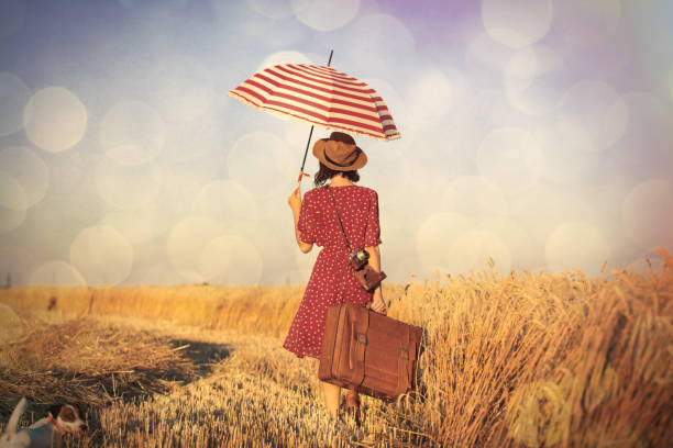 photo of beautiful young woman with umbrella, retro camera and suitcase on the wonderful field and sky background