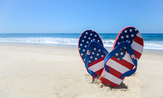 Patriotic USA background with flip flops and decorations on the sandy beach