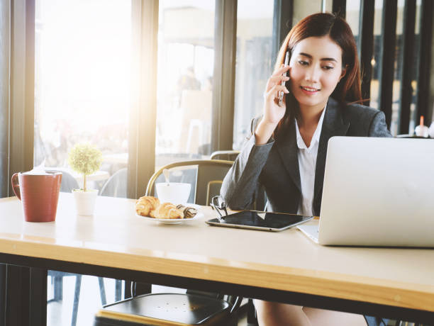 istock Charming businesswoman talking with smartphone and look at laptop while working at cafe. Work out office concept. 688355316