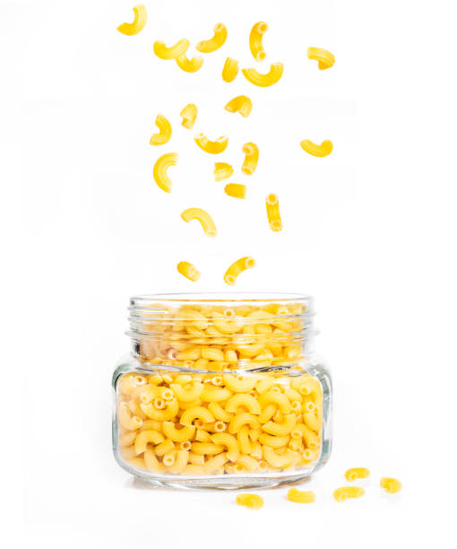 pâtes macaroni crus en pot de verre transparent avec des morceaux tomber vers le bas dans le bocal et certains sur le terrain, sur fond blanc isolé - macaroni photos et images de collection