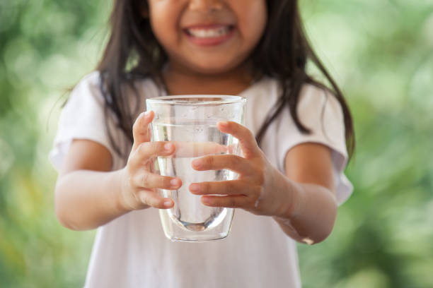 Cute asian little girl holding glass of fresh water in green nature background stock photo