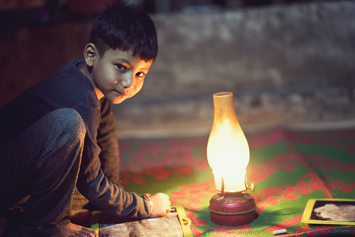 Portrait of rural Indian boy studying under oil lamp