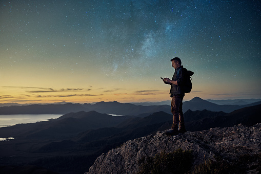 Shot of a young hiker using a tablet while standing at the top of a mountain at dusk