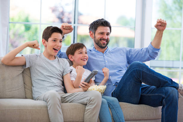 istock Father and sons watching tv at home 688438550