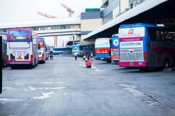 Thai girl with luggage is walkign between parked buses in station Moh Chit 2 at early morning. Woman has also a soft toy. Moh Chot 2 is one of big bus terminals in Bangkok.