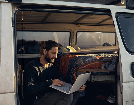 Cropped shot of a young man using a laptop while on a roadtrip