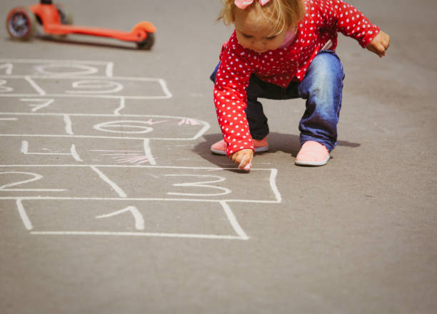 bambina che gioca hopscotch nel parco giochi - little girls sidewalk child chalk foto e immagini stock
