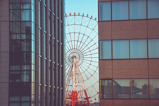 View of Ferris wheel between modern building in the town's pedestrian zone in Odaiba, skyline is sunset at Tokyo, Japan.