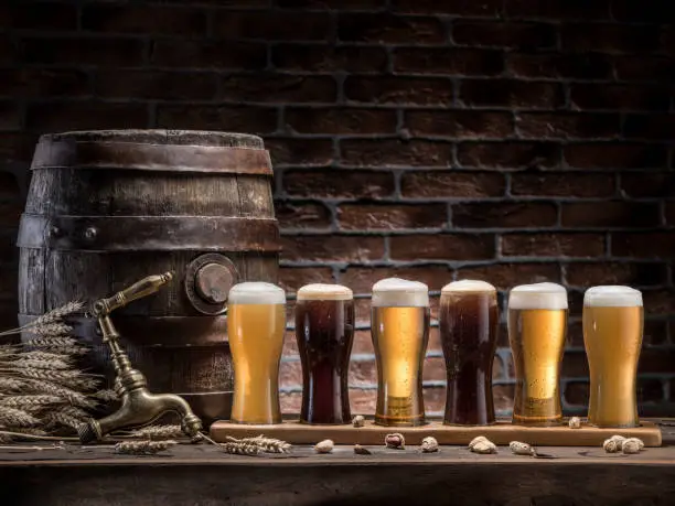 Glasses of beer and ale barrel on the wooden table. Craft brewery.