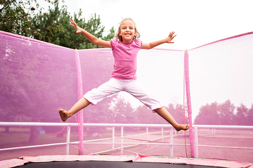 Happy caucasian girl jumping high on a trampoline ona a sunny day outdoors.