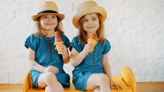 Two little girls eat ice cream at home while waiting for a summer vacation