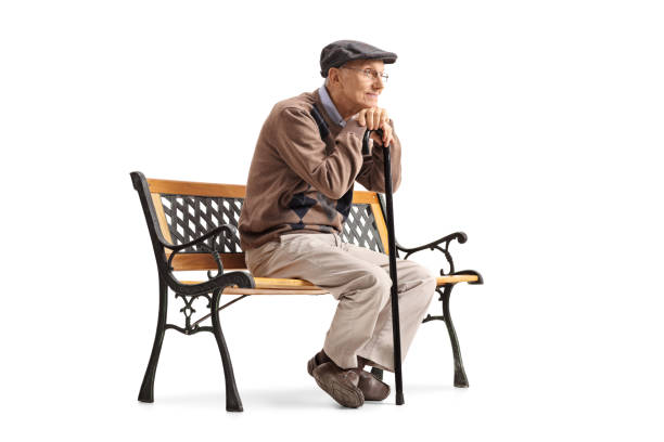 Pensive senior with a walking cane sitting on a bench isolated on white background