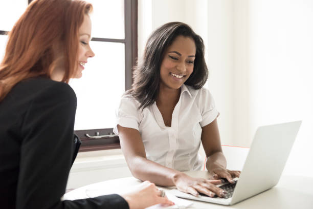 istock Young businesswoman using laptop and smiling, colleague watching 688468780