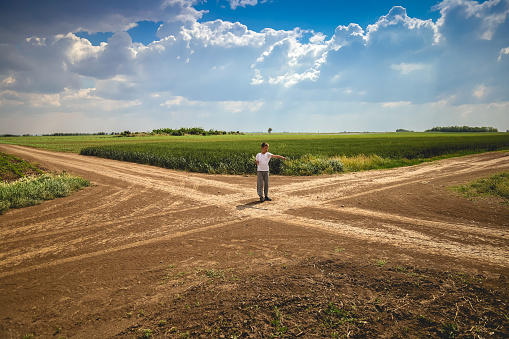 8 year boy standing at crossroad in path and pretending to regulate invisible traffic. Crossroad is surrounded by vast fields of wheat, rye and corn.