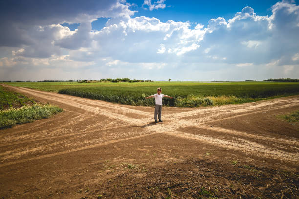 Boy Standing at Crossroad in Path 8 year boy standing at crossroad in path and pretending to regulate invisible traffic. Crossroad is surrounded by vast fields of wheat, rye and corn. fork in the road stock pictures, royalty-free photos & images