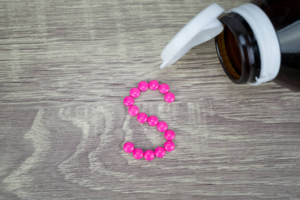 istock Pink pills forming shape to S alphabet on wood background 688478904