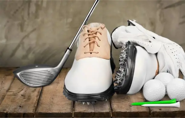 A pair of golfing shoes and a golf club on  background