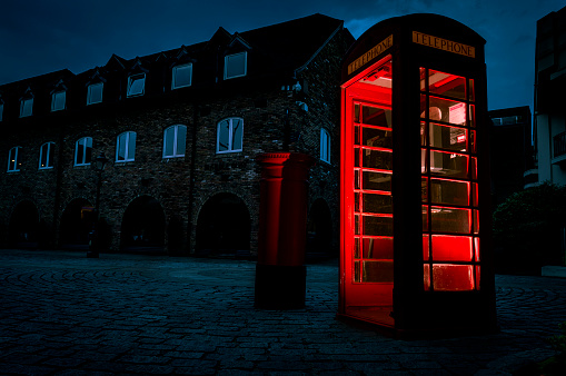 Atmospheric image of telephone box or phone booth in the street with historical architecture at night in London, England, UK