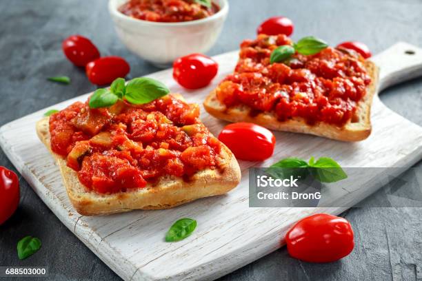 Fresh Homemade Crispy Italian Appetizer Bruschetta Topped With Tomato Eggplant Zucchini Yellow Pepper Garlic And Basil On White Wooden Board Healthy Food Stock Photo - Download Image Now