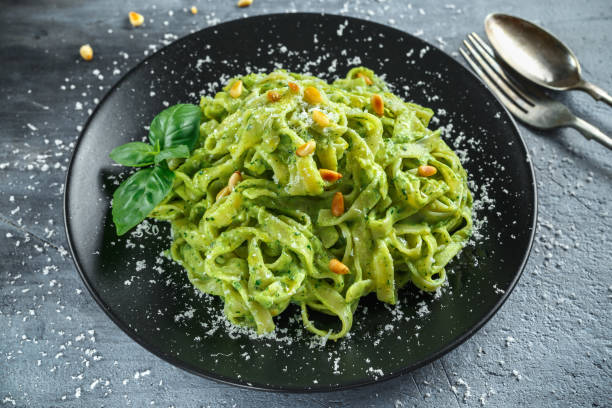 istock Tagliatelle pasta with pesto sauce, pine nuts and parmesan on black plate. 688512494