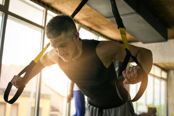 Young man workout in healthy club. Man doing exercise with strip  system. Young man workout in healthy club. Man doing exercise with strip  system. suspension training stock pictures, royalty-free photos & images