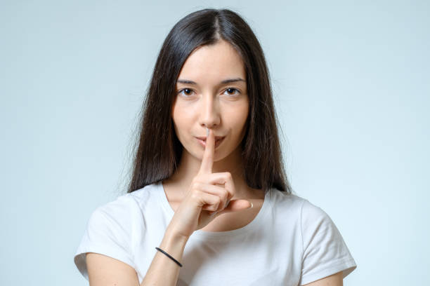 istock Keep silence! Beautiful young woman holding finger on lips and looking at camera isolated on white 688525928