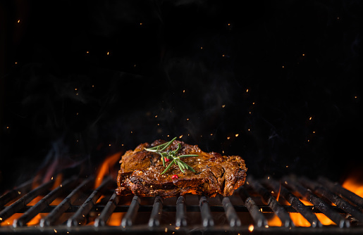 Beef steak on the grill grate, flames on background. Barbecue and grill, delicious food.
