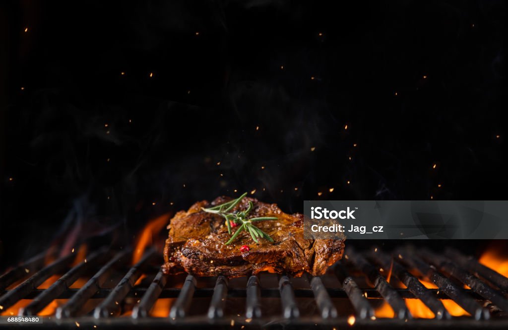 Beef steak on the grill grate, flames on background Beef steak on the grill grate, flames on background. Barbecue and grill, delicious food. Barbecue - Meal Stock Photo