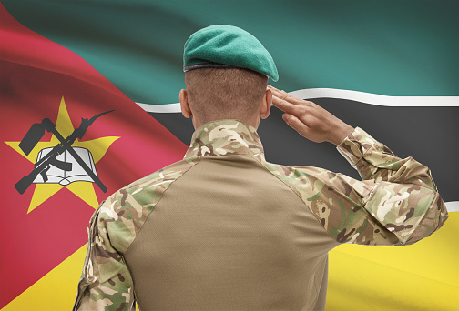 Dark-skinned soldier in hat facing national flag series - Mozambique