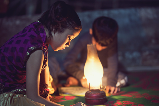 Rural girl and boy studying under illuminated oil lamp