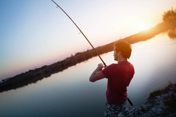 istock Young man fishing on lake at sunset enjoying hobby 688564654