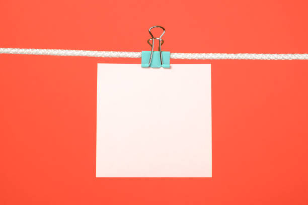 istock Blank pink paper note on clothesline over red background 688577758