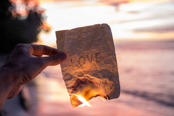 mano que sostiene un papel quemado con la palabra amor - crumpled paper document frustration fotografías e imágenes de stock