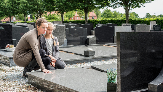 mother and daughter visiting grave of deceased family at the cemetery