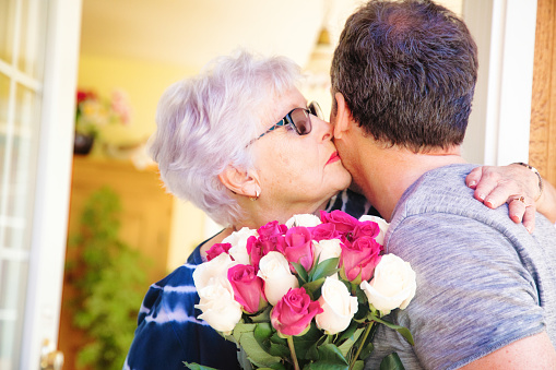 Senior woman kisses mature son bringing bouquet of roses