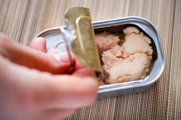 istock Woman fingers opening tin can with cod liver. 688603856